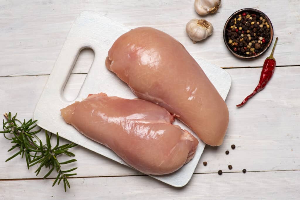 Raw uncooked chicken breast with cooking ingredients on a wooden background