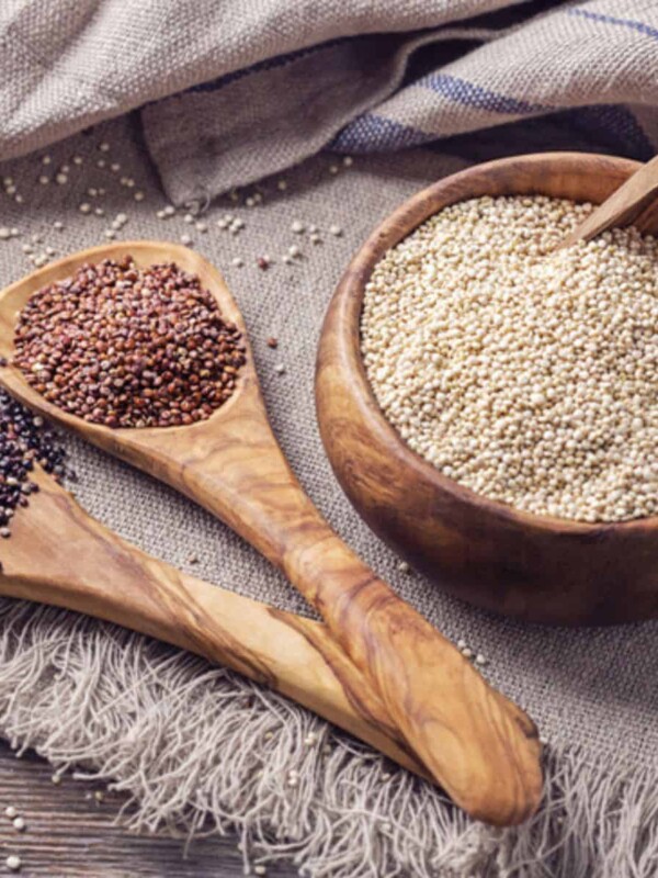 On a piece of cloth, some wooden pots contain quinoa seeds. There are different types of seeds: white, brown, and black quinoas.