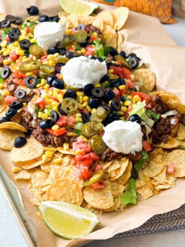 A big tray loaded with tortilla chips, beef and beans mix, colorful veggies and topped with sour cream.
