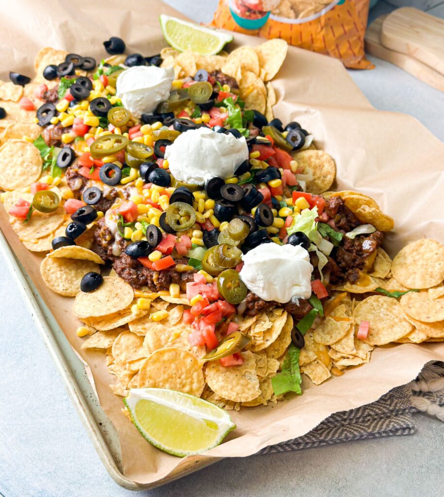 Loaded Taco Nachos prepared on a big tray loaded with tortilla chips, beef and beans mix, colorful veggies and topped with sour cream.