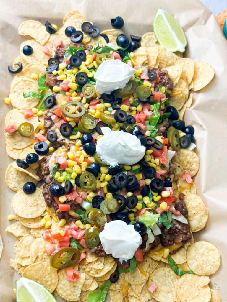A big colorful tray loaded with tortilla chips, beef and beans mix, colorful veggies and topped with sour cream.