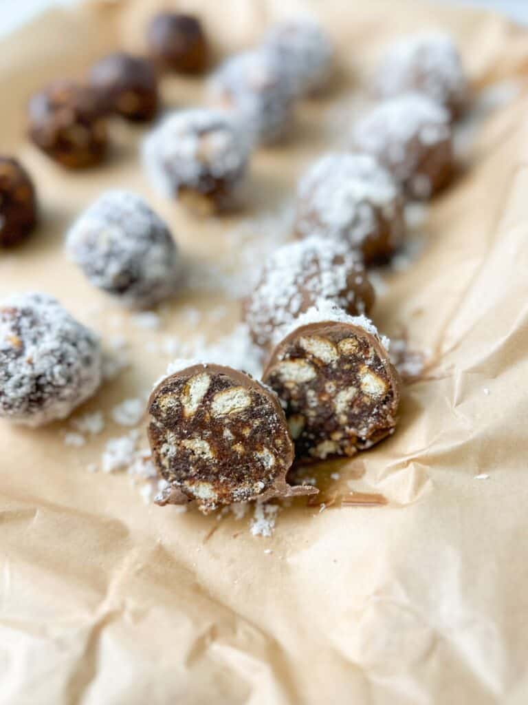 Chocolate date balls are covered with coconut, and one of them is cut in half.