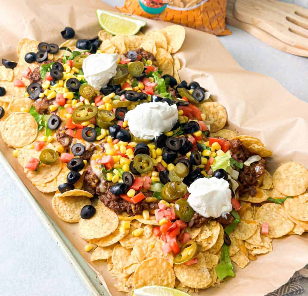 Loaded Taco Nachos served on a big tray loaded with tortilla chips, beef and beans mix, colorful veggies and topped with sour cream.