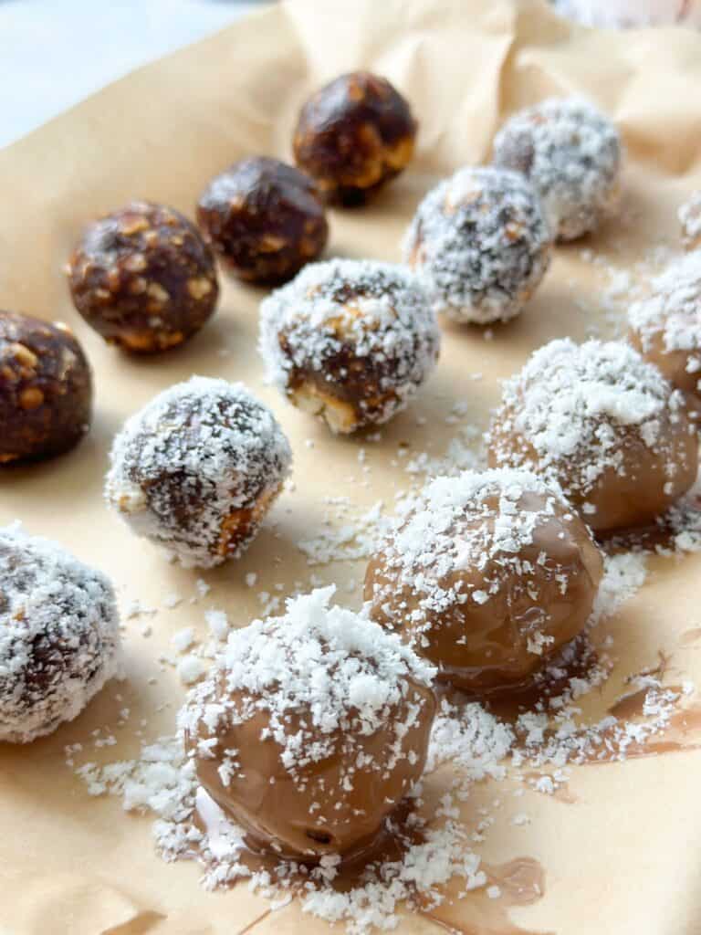 Date balls are covered with chocolate and sprinkled with coconut.