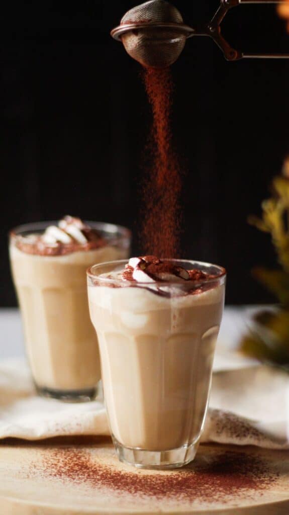 sift cocoa powder on top of two glasses of peanut butter coffee topped with whipped cream