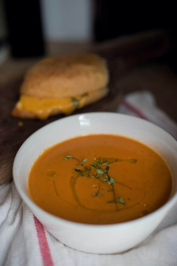 a bowl of tomato soup that is served with an air-fried grilled cheese sandwich in the background
