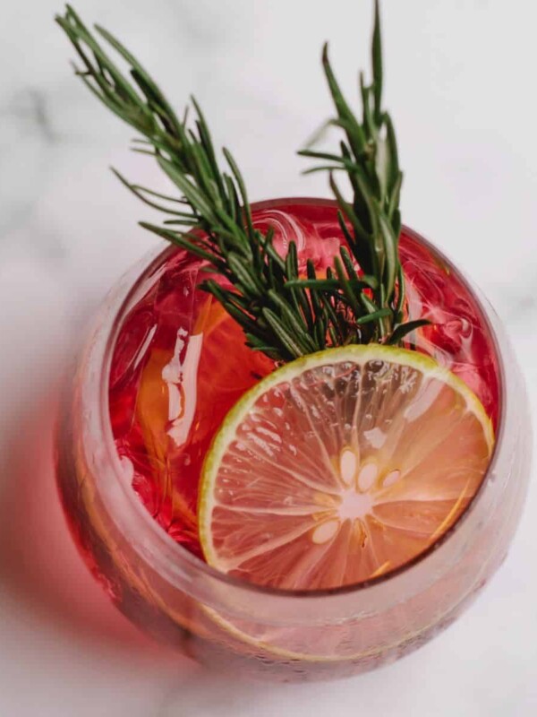 A cup of natural healing cough syrup topped with lemon and rosemary.