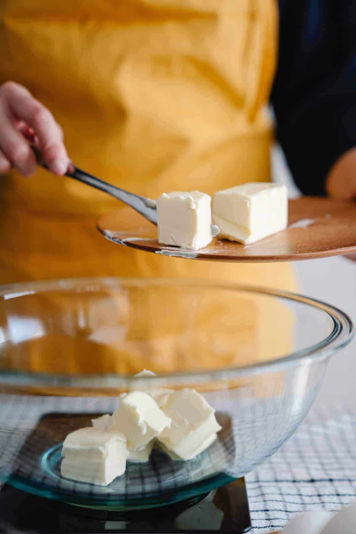 pieces of softened butter being added to a large mixing bowl