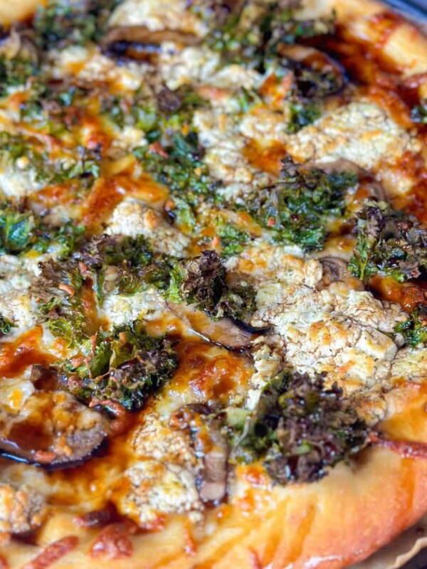 Pizza with a golden brown crust with kale, mushroom, and goat cheese. The pizza is garnished with balsamic glaze.