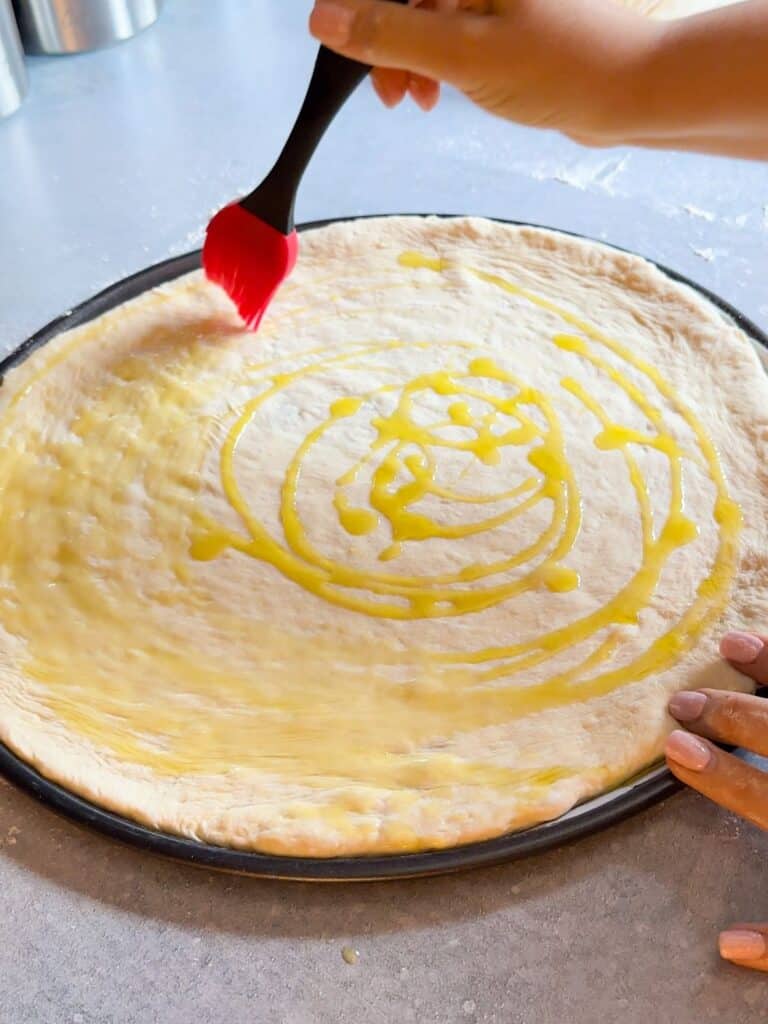 Olive oil is drizzled on the stretched dough before adding the toppings.