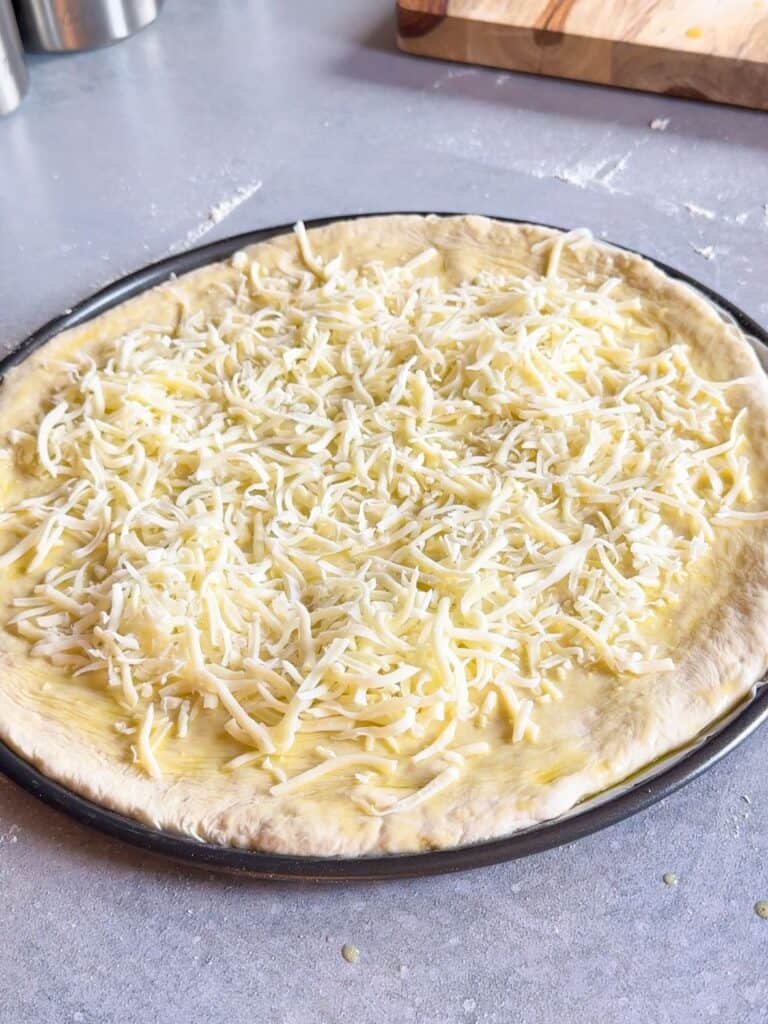 Shredded mozzarella is generously and evenly added on top of the dough.