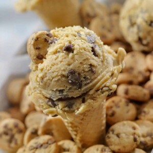 A cone of cookie dough ice cream surrounded by cookies in the background.