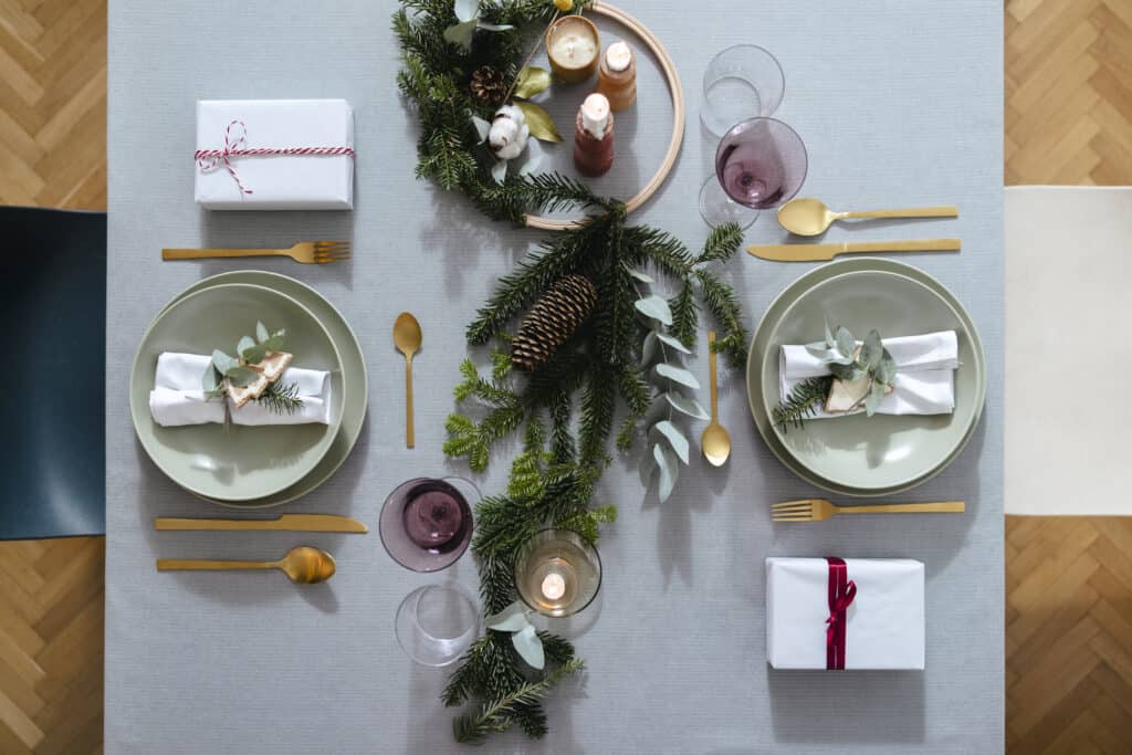 Beautiful table setting with golden cutlery and green porcelain plate on a gray table with Christmas decoration and presents.