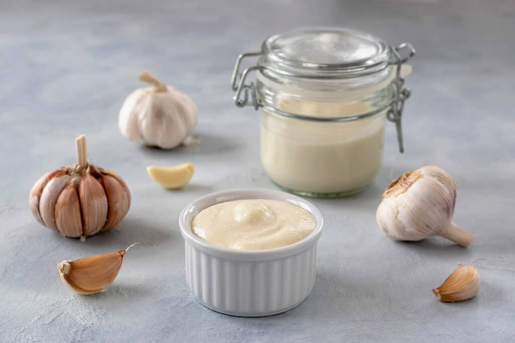 Lebanese garlic sauce in a jar and a saucer and some garlic cloves