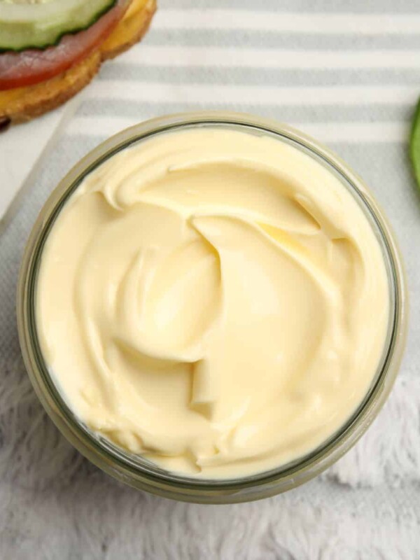 a jar of delicious homemade mayonnaise near fresh sandwich on table