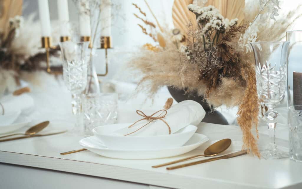 luxury table settled up with plates, crystal glasses, napkins, golden eating utensils, and golden candlestick holders for the best hosting