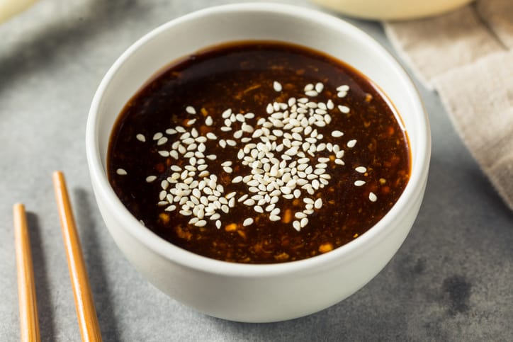 Homemade soy dipping sauce with sesame in a white bowl next to two sushi sticks