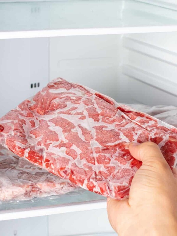 Closeup of hand choosing fresh raw meat in the freezer.