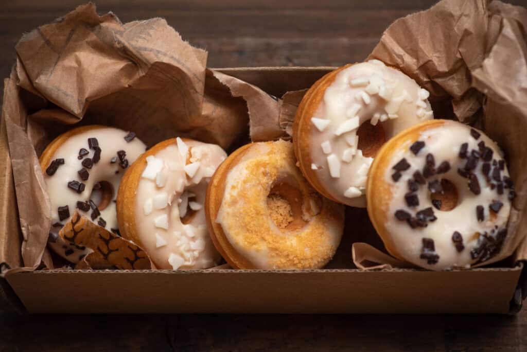 White glazed mini donuts in a box. White mini donuts decorated with white and dark chocolate on a wooden background. Delicious, sweet food.