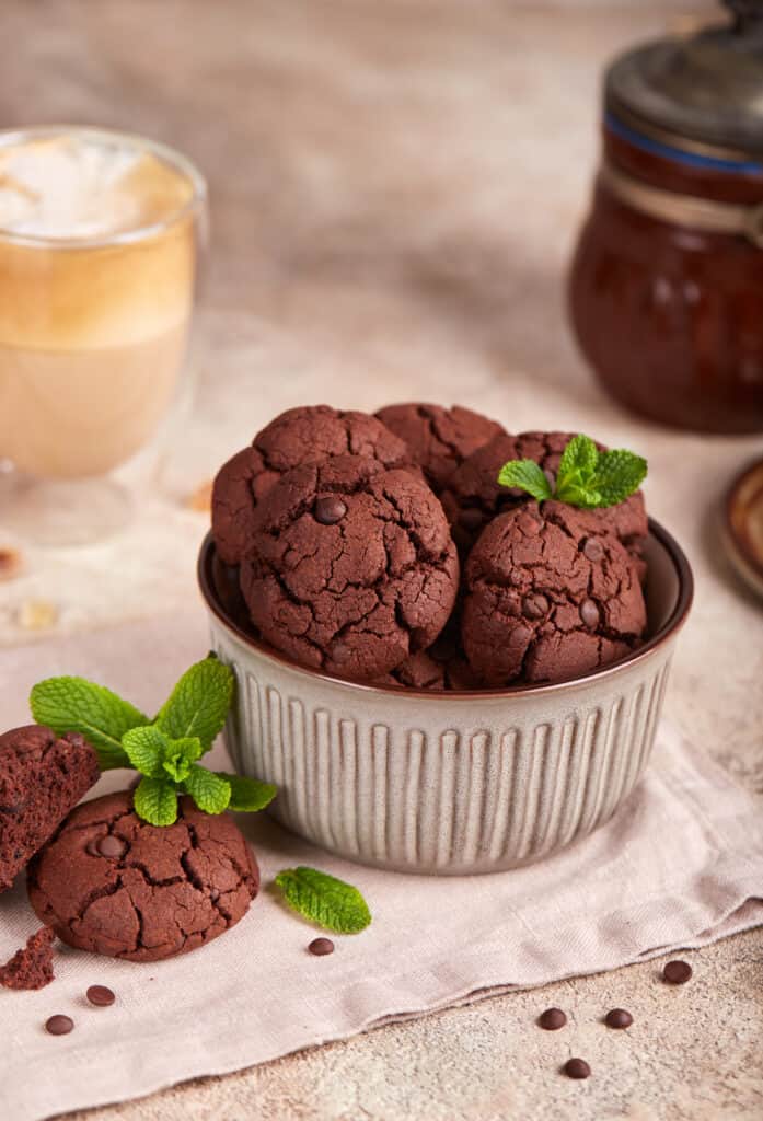 a batch of Nutella cookies served in a small stainless steel bowl with fresh mint leaves on the top with chocolate chips and cracks.