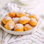 A white bowl filled with golden donut holes dusted with powdered sugar.