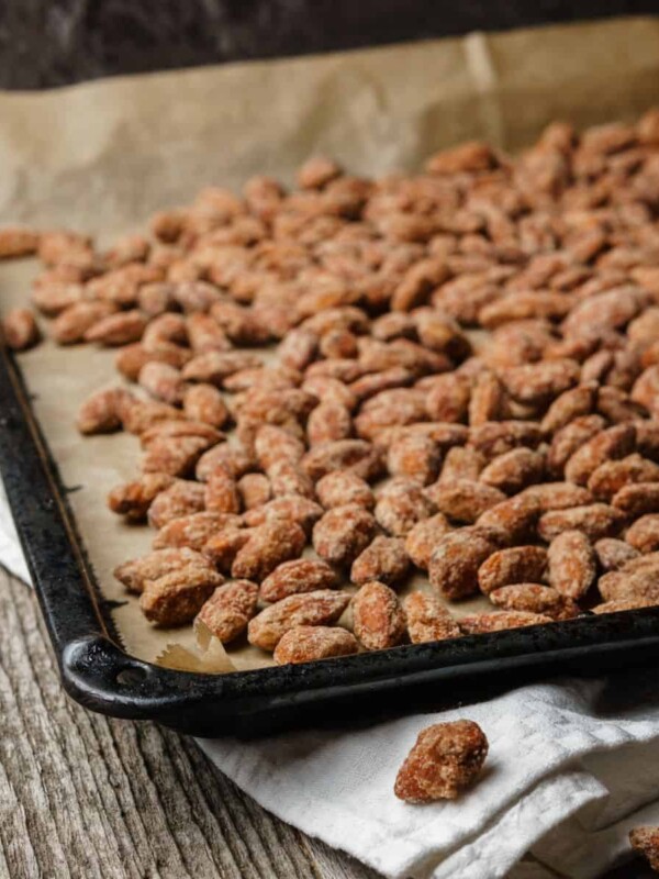 Roasted almonds outspread on black baking tray, paper, white cloth on rustic textured wooden table