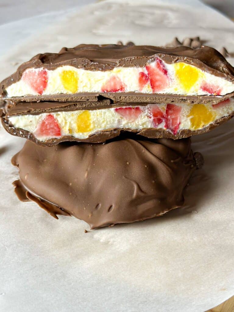 Close photo of two halves of a chocolate covered bar, showing the inside filling of yogurt, strawberries, and mango. 
