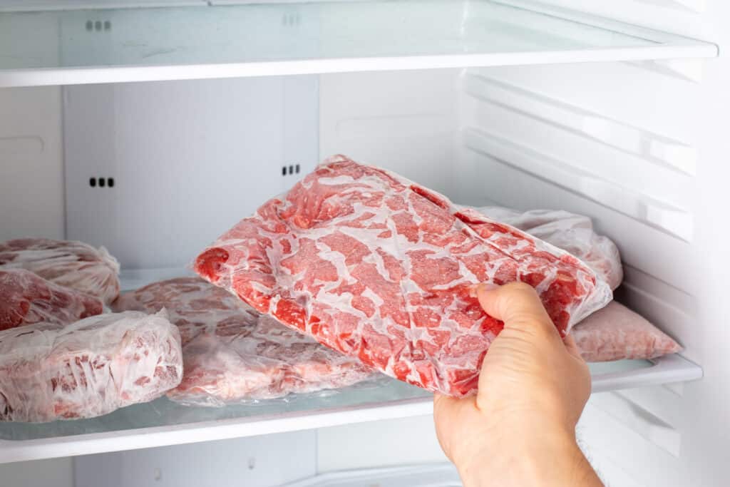 Closeup of hand choosing fresh raw meat in the freezer. Frozen food