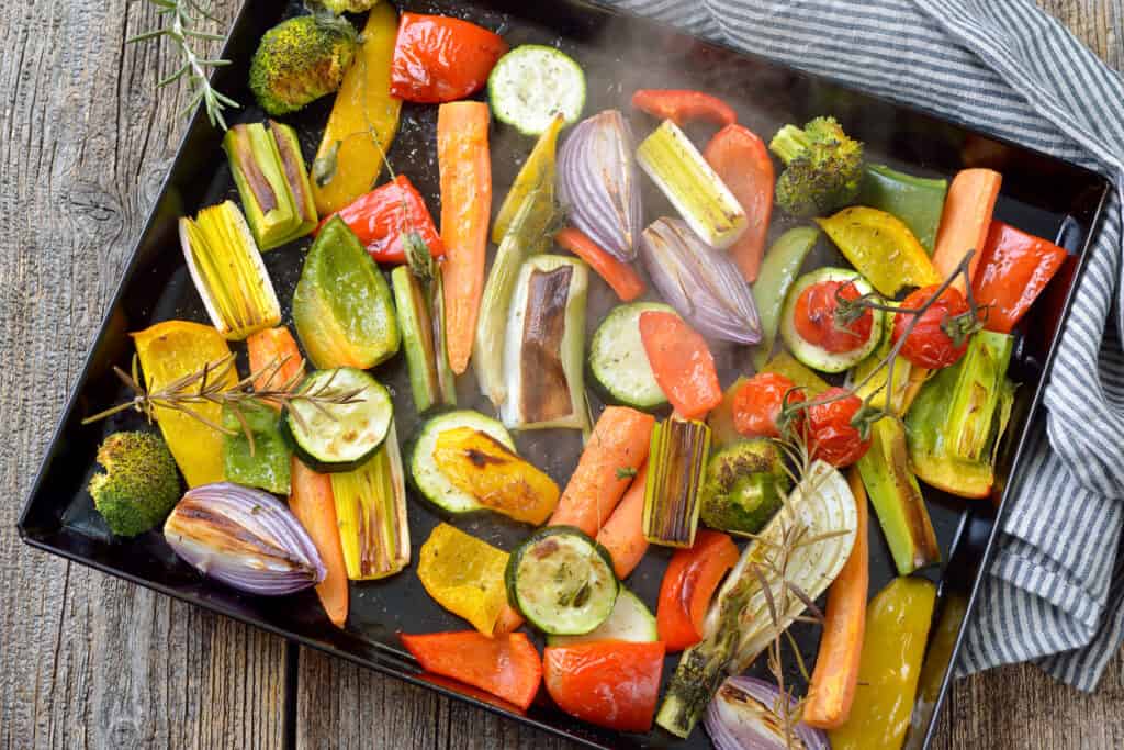 Baked mixed colorful vegetables on a baking sheet  just coming steaming out of the oven