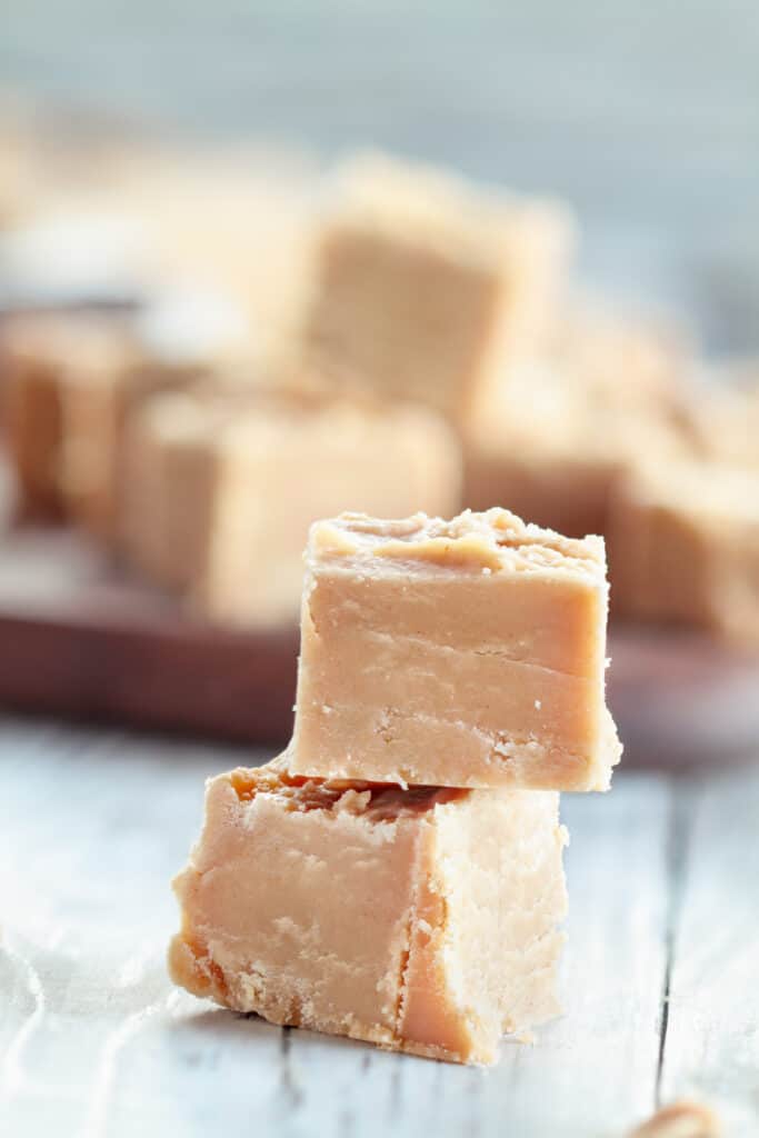 Squares of delicious, homemade peanut butter fudge over a rustic wood table background with blurred background.