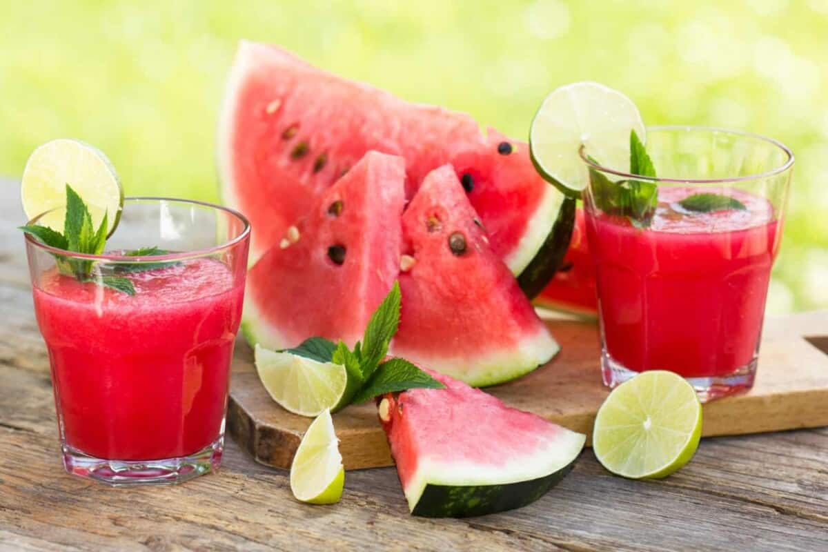 healthy refreshing watermelon recovery juice served in two cups decorated with lemon wedges and fresh mint leaves alongside watermelon slices