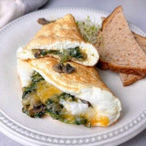 This amazing egg white vegetable omelet is topped with cheese, spinach, mushrooms, onion, and pepper and is served with some toast.