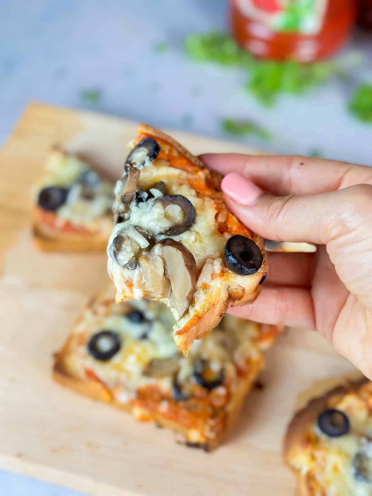 a hand holding a piece of delicious pizza toast with a soft, chewy interior and a delicate, crispy exterior