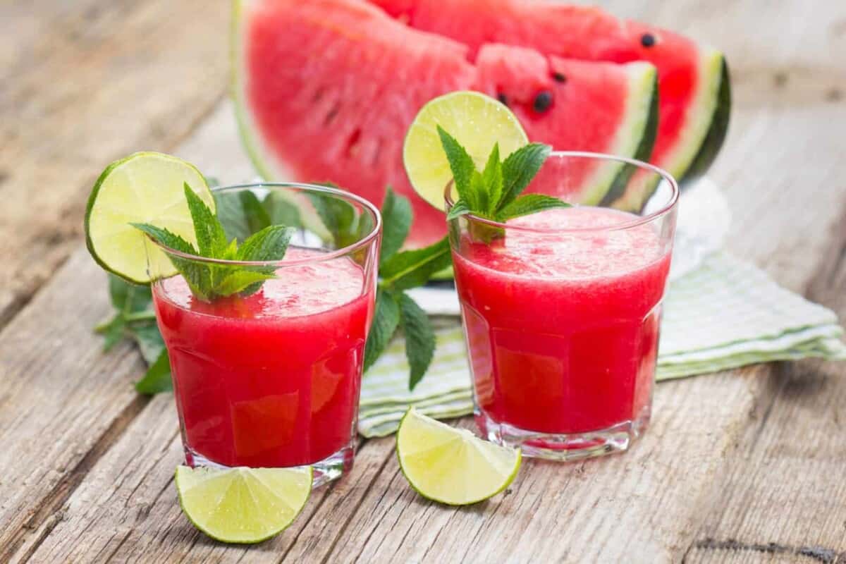 watermelon recovery juice served in two cups decorated with lemon wedges and fresh mint leaves