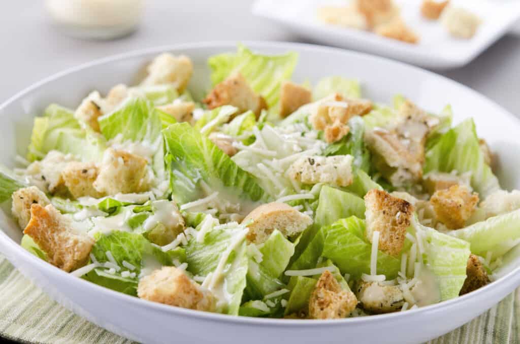 Closeup of a fresh caesar salad, with romaine lettuce hearts, croutons, parmesan cheese and dressing.  Dressing and croutons.