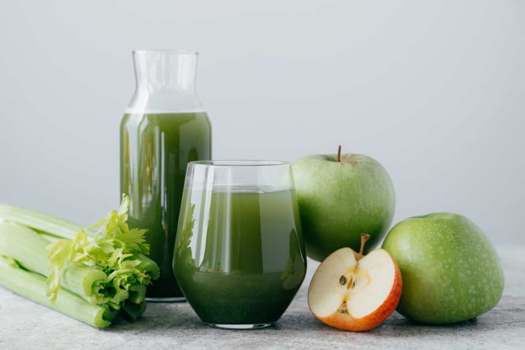 Photo of green smoothie with celery and apple in two glass containers on white background. Healthy organic juice. Dieting concept.