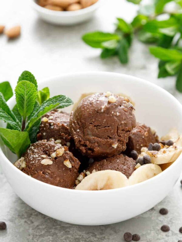 a bowl of chocolate and banana fruit ice cream garnished with with almond nuts and decorated with fresh mint leaves
