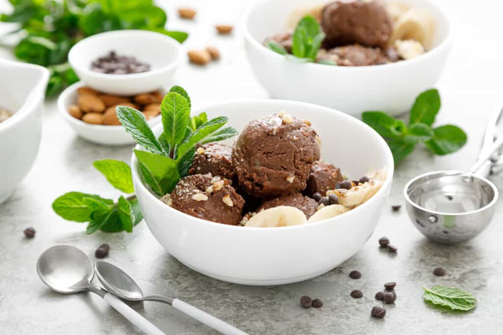 two bowls of chocolate and banana fruit ice cream garnished with with almond nuts and decorated with fresh mint leaves
