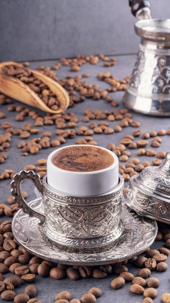Turkish coffee with traditional copper serving set. Cup of coffee and traditional delight. Coffee beans on the floor. Assorted traditional turkish coffee in metal traditional cup.