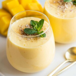 two cups of mango lassi drink with mint leaves on top