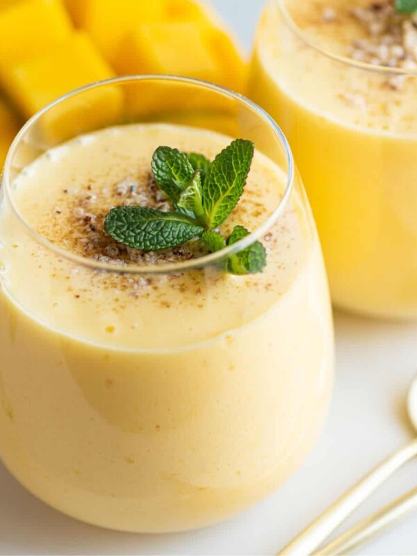two cups of mango lassi drink with mint leaves on top