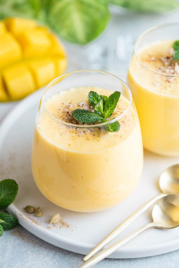 two cups of mango lassi garnished with fresh mint and ground cardamom