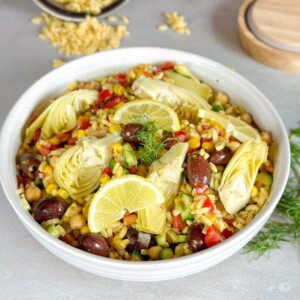 a white bowl of Mediterranean Orzo Pasta Salad topped with artichoke and lemon wedges