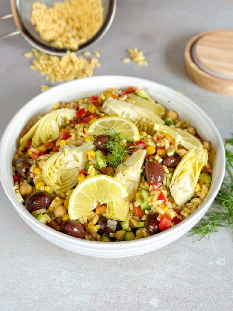 a white bowl of Mediterranean Orzo Pasta Salad topped with artichoke and lemon wedges