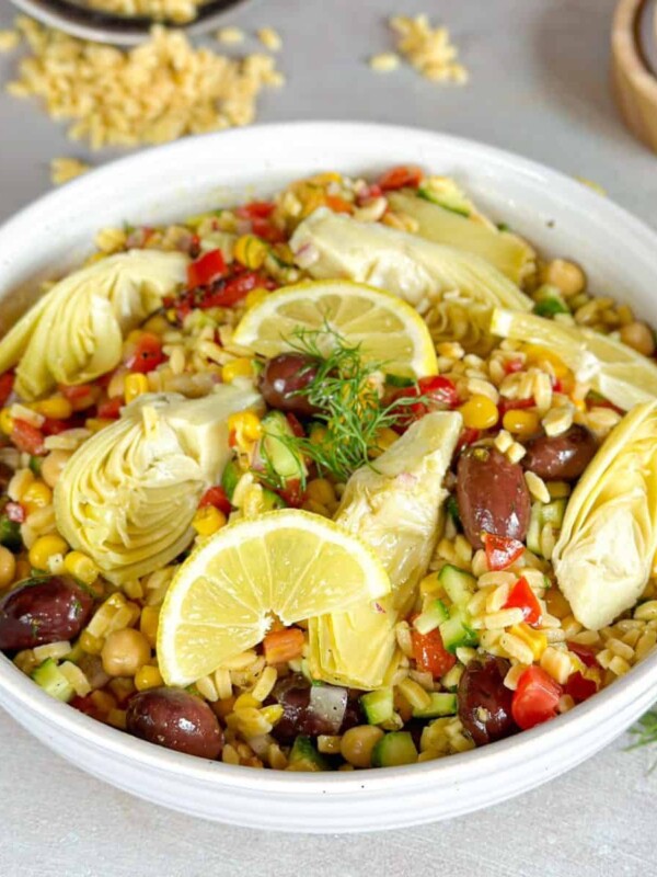 a bowl of Orzo Pasta Salad topped with artichoke and lemon wedges