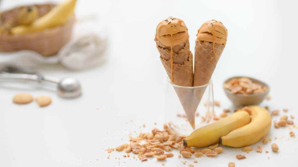 Cropped shot of summer dessert with peanut butter banana flavor ice-cream cones, topping 