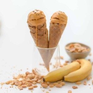 two cones of peanut butter ice cream palced in a cup next to bananas and pesnuts