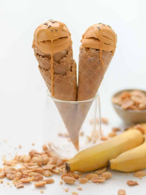 two cones of peanut butter ice cream palced in a cup next to bananas and pesnuts