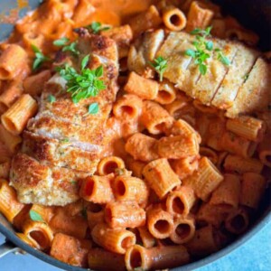 a bowl of rigatoni pasta with pink sauce topped with chicken breasts