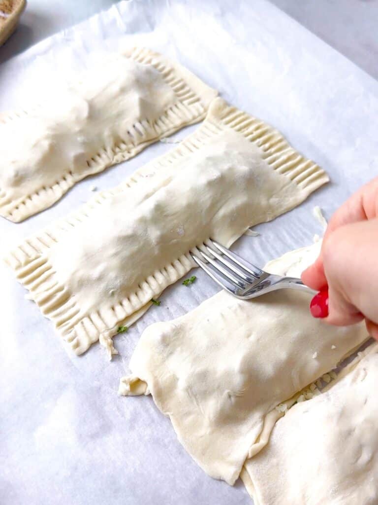 a woman pressing the fork on the puff pastry rectangles